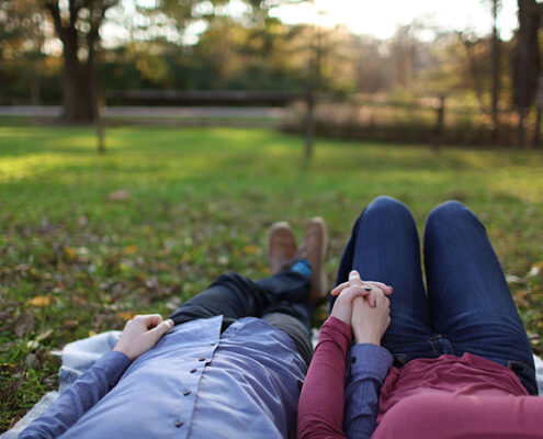 A couple holding hands and laying on the grass in a park