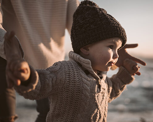 A person holding the hands of a young child as they walk.