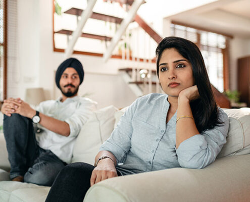 A couple sitting on a couch looking sad.